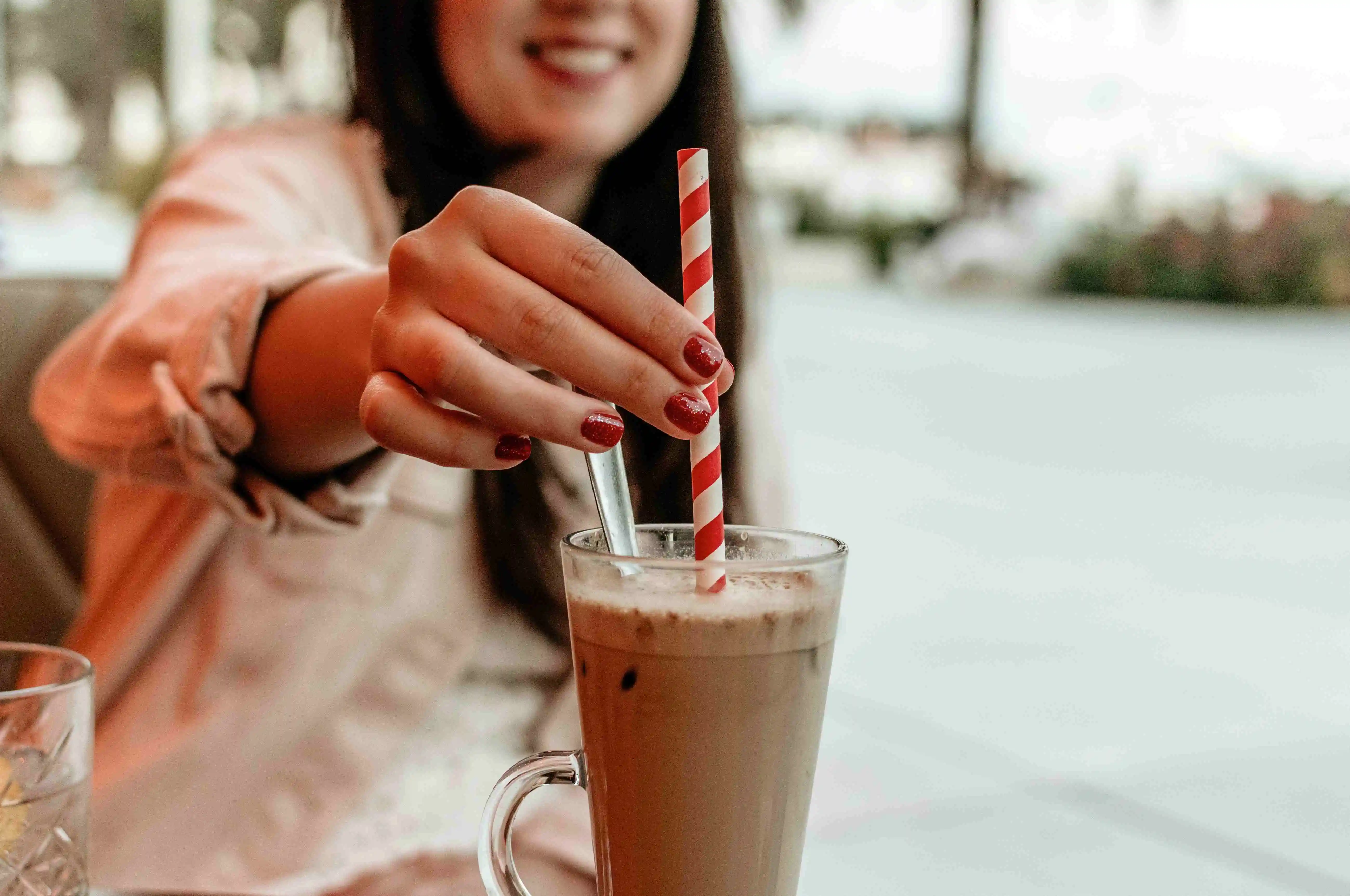 woman holding drinking straw in glass of coffee